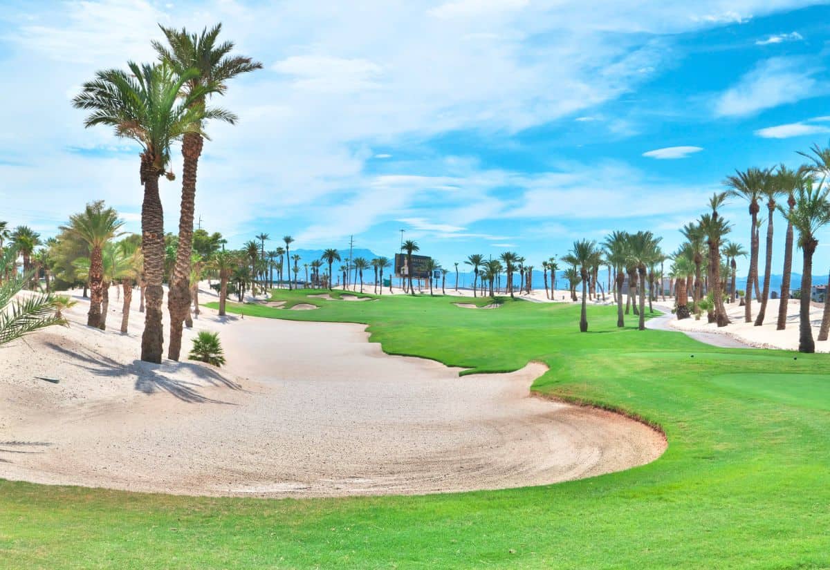 A golf course with green fairways, sand bunkers, and numerous palm trees under a bright blue sky.